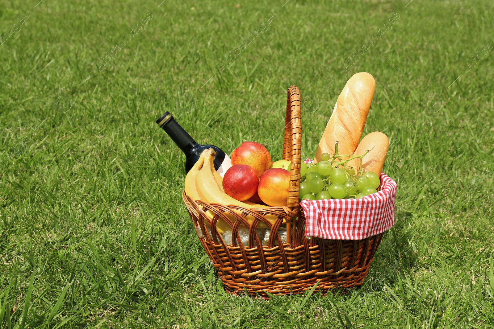 Photo of Basket with food and bottle of wine on lawn in park. Summer picnic