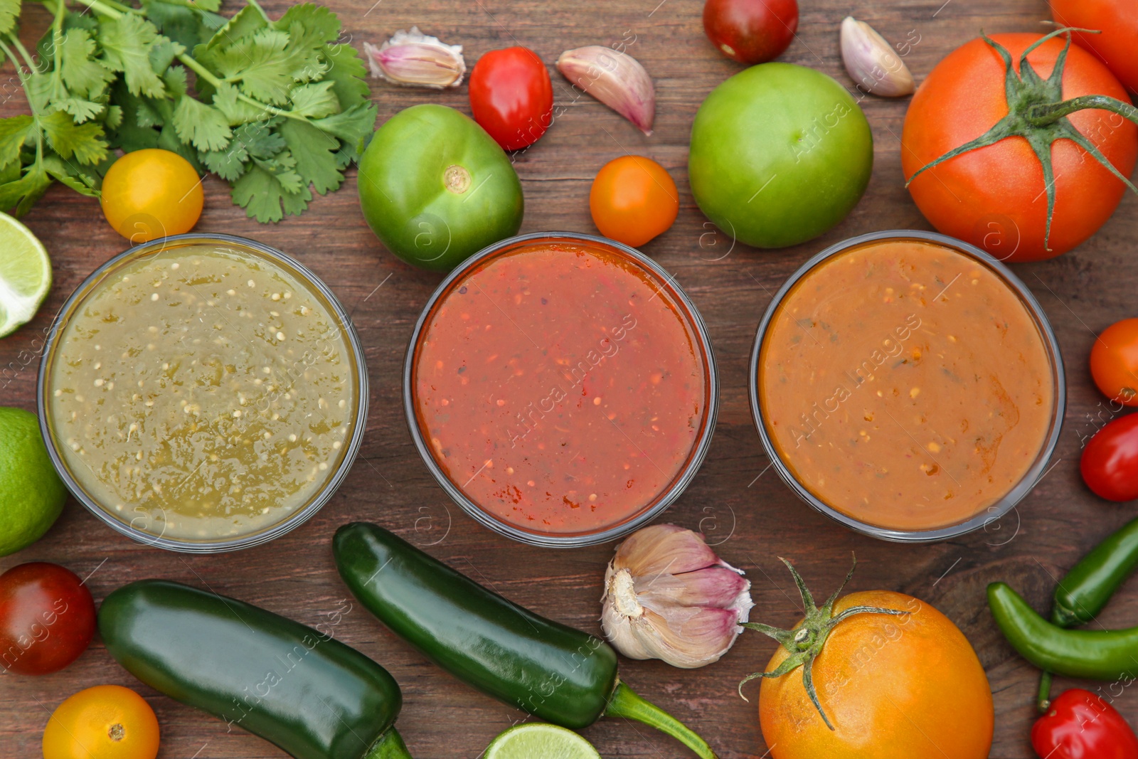 Photo of Flat lay composition of tasty salsa sauces and different ingredients on wooden table