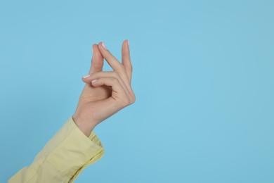 Photo of Woman snapping fingers on light blue background, closeup of hand. Space for text