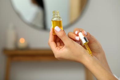Photo of Young woman applying essential oil on wrist indoors, closeup