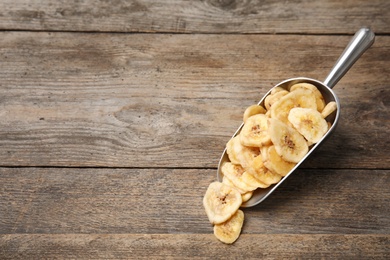Photo of Scoop with banana slices on wooden background, space for text. Dried fruit as healthy snack
