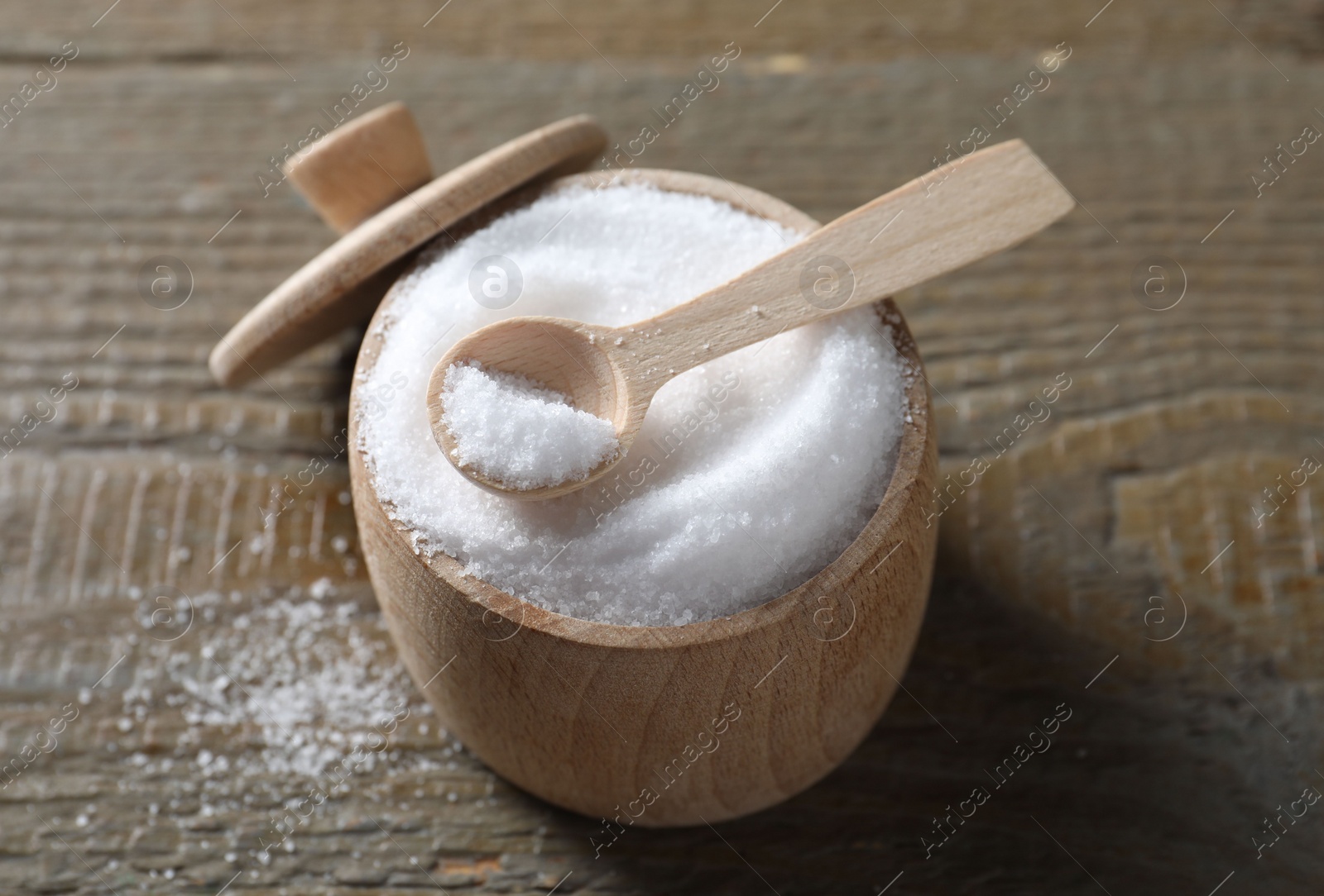 Photo of Organic salt in bowl and spoon on wooden table, closeup