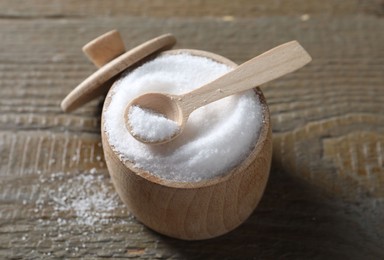 Photo of Organic salt in bowl and spoon on wooden table, closeup