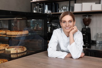 Professional baker at cashier desk near showcase in store