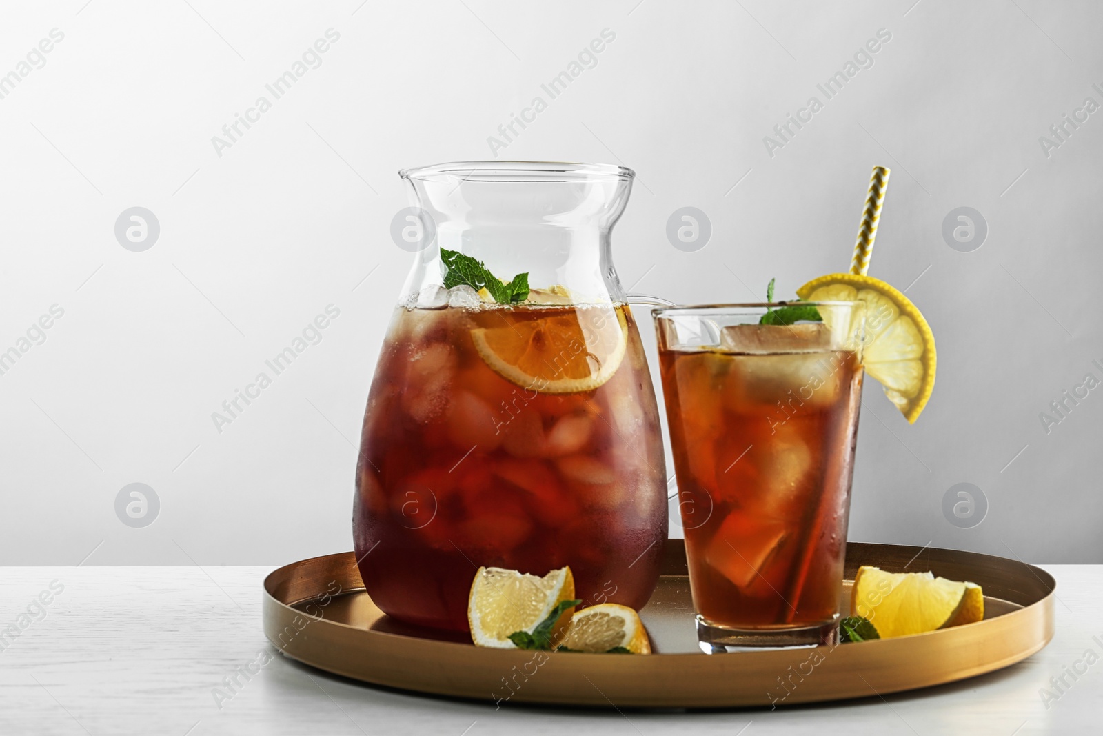 Photo of Jug and glass of delicious iced tea on table against light background