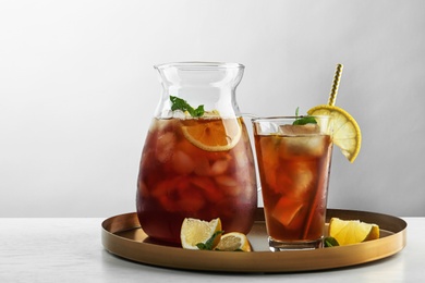 Photo of Jug and glass of delicious iced tea on table against light background