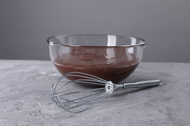 Whisk and bowl with chocolate cream on table against grey background