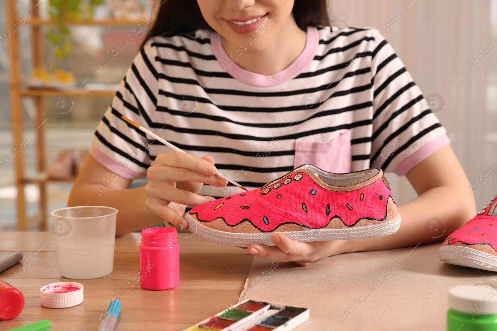 Photo of Woman painting on sneaker at wooden table indoors, closeup. Customized shoes