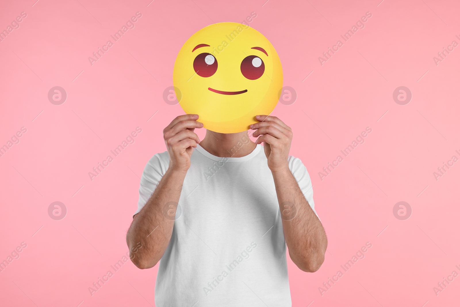 Photo of Man covering face with smiling emoticon on pink background