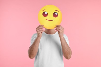 Photo of Man covering face with smiling emoticon on pink background