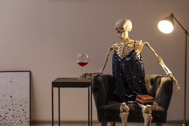 Skeleton in dress with wine sitting at table indoors