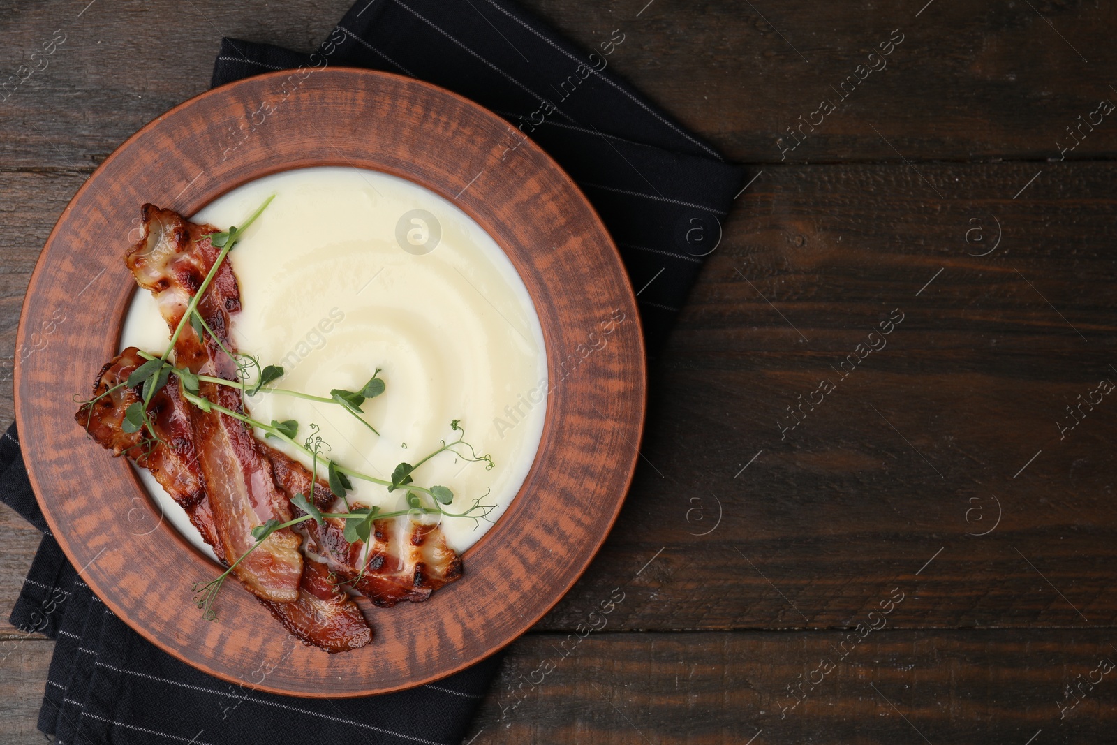 Photo of Delicious potato soup with bacon and microgreens in bowl on wooden table, top view. Space for text