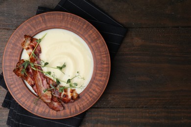 Photo of Delicious potato soup with bacon and microgreens in bowl on wooden table, top view. Space for text