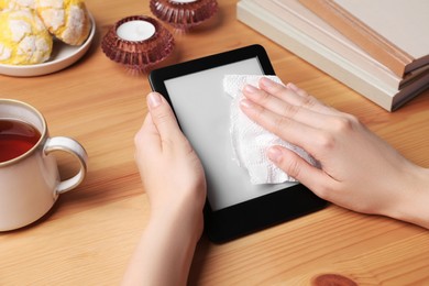 Woman wiping smartphone with paper at wooden table, closeup