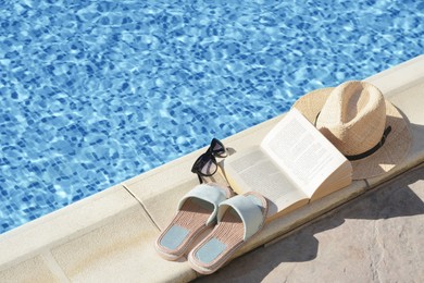 Photo of Stylish sunglasses, slippers, straw hat and book at poolside on sunny day, space for text. Beach accessories