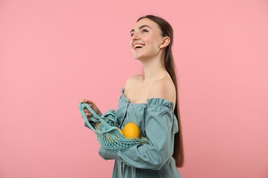 Woman with string bag of fresh lemons on pink background