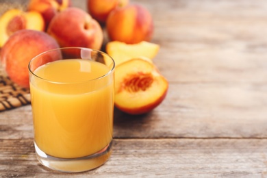 Photo of Natural peach juice and fresh fruits on wooden table. Space for text