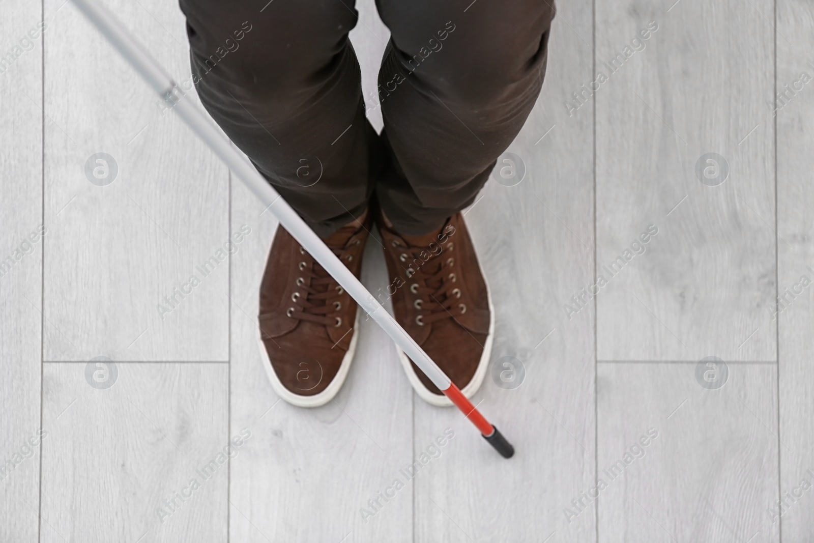 Photo of Blind person with long cane standing indoors, top view