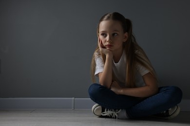 Sad girl sitting on floor near dark grey wall indoors, space for text