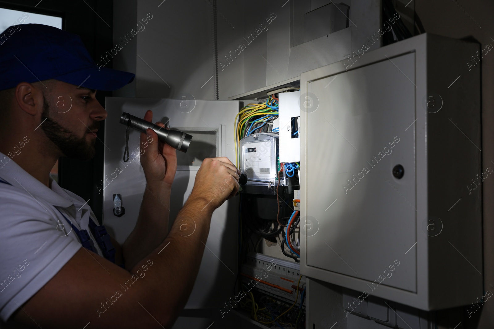Photo of Electrician with flashlight fixing electric panel indoors