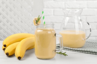 Photo of Mason jar and jug of tasty banana smoothie with fresh fruits on white marble table