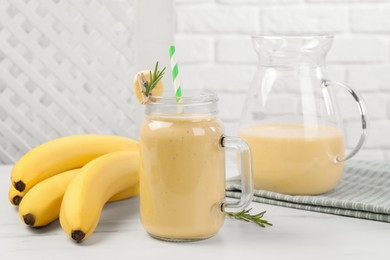 Mason jar and jug of tasty banana smoothie with fresh fruits on white marble table