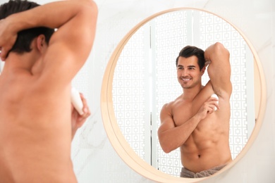 Photo of Handsome young man applying deodorant in bathroom