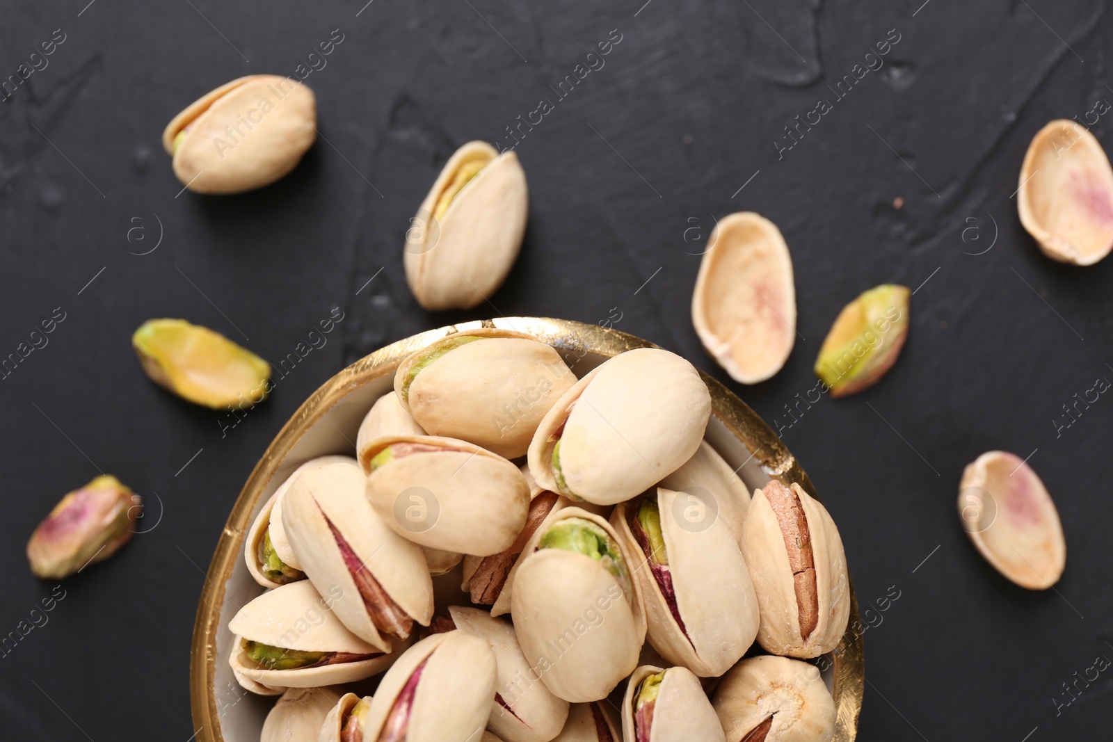 Photo of Tasty pistachios in bowl on black table, top view