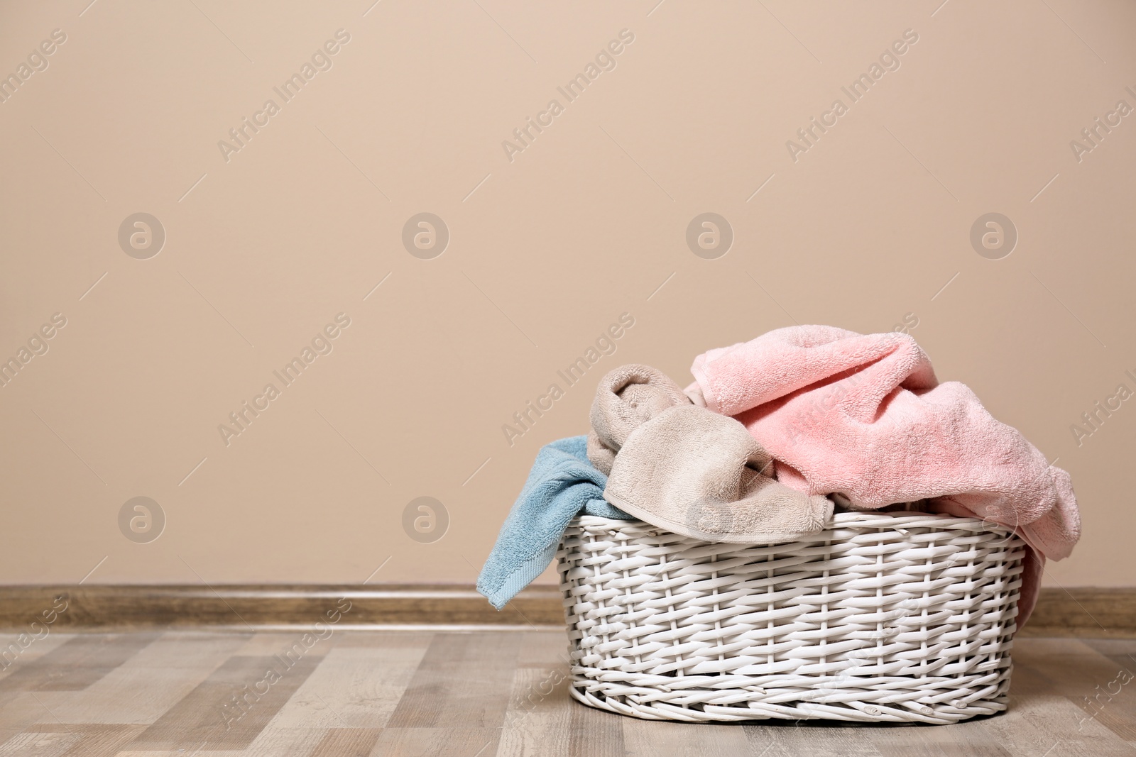 Photo of Laundry basket with dirty clothes on floor indoors. Space for text