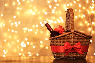 Photo of Gift basket with bottle of wine against blurred lights. Space for text