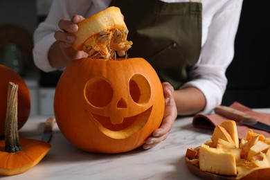 Photo of Woman with carved pumpkin for Halloween at white marble table, closeup