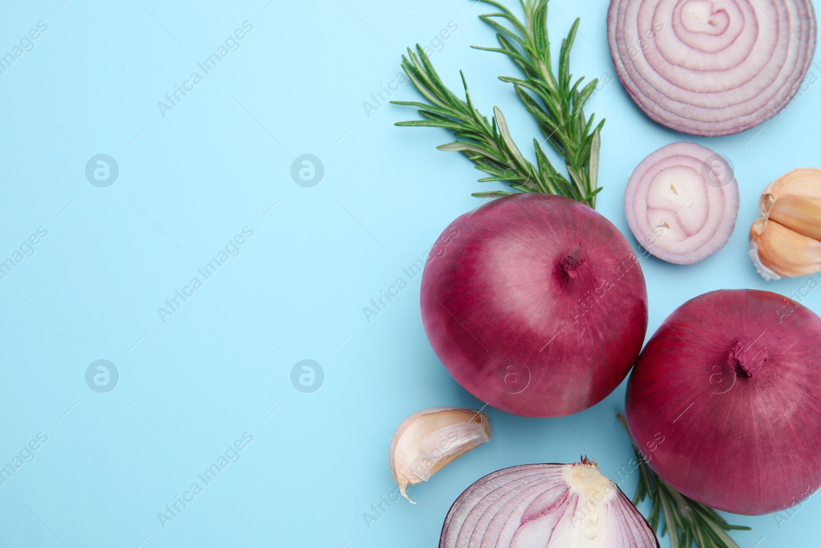 Photo of Fresh red onions, garlic and rosemary on light blue background, flat lay. Space for text