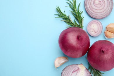 Photo of Fresh red onions, garlic and rosemary on light blue background, flat lay. Space for text