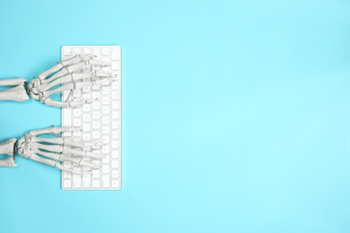 Photo of Human skeleton using computer keyboard on light blue background, top view. Space for text