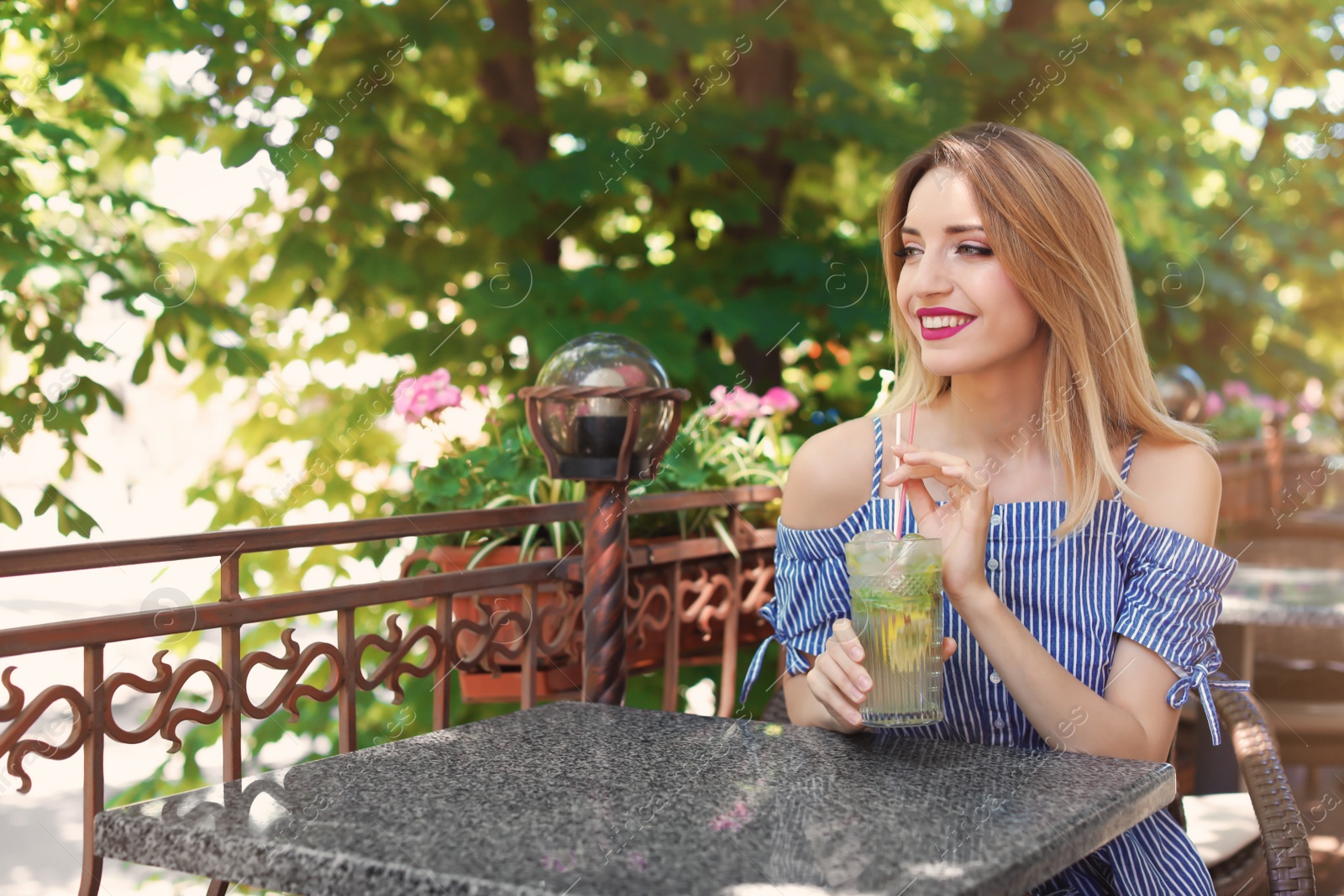 Photo of Young woman with glass of tasty lemonade at table in cafe, outdoors. Natural detox drink