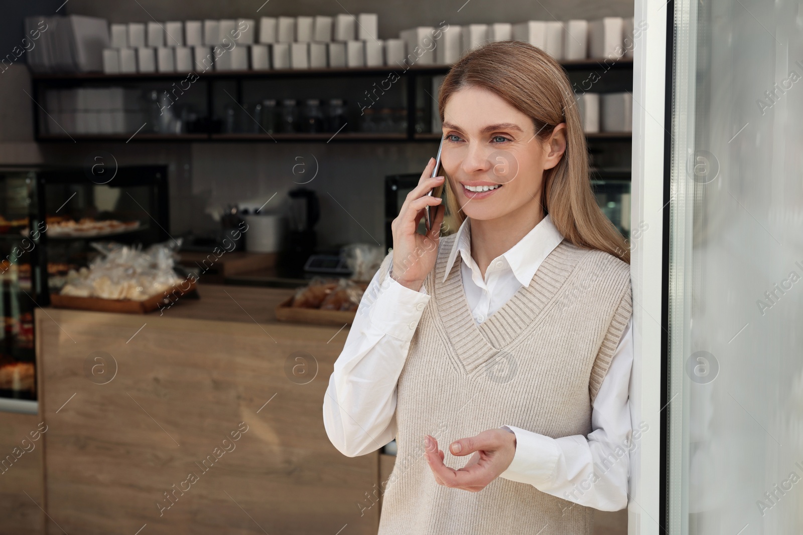 Photo of Happy business owner talking on phone in bakery shop. Space for text