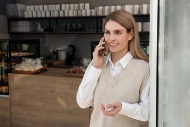 Photo of Happy business owner talking on phone in bakery shop. Space for text