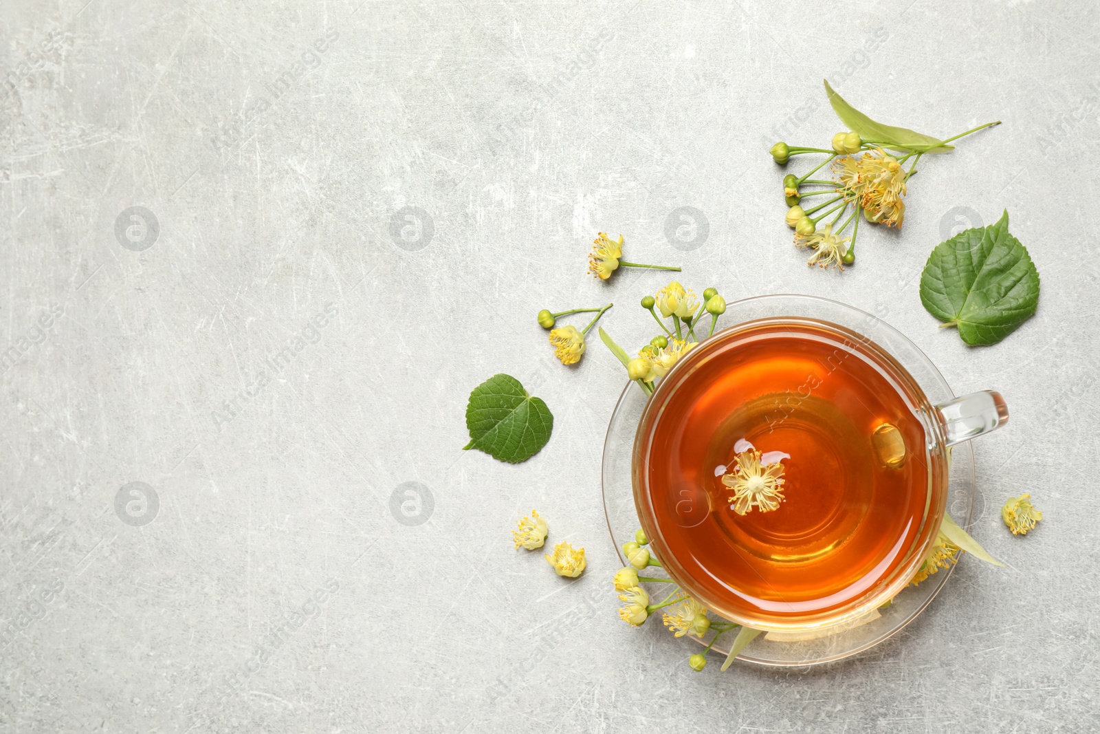 Photo of Cup of tea and linden blossom on light grey table, flat lay. Space for text