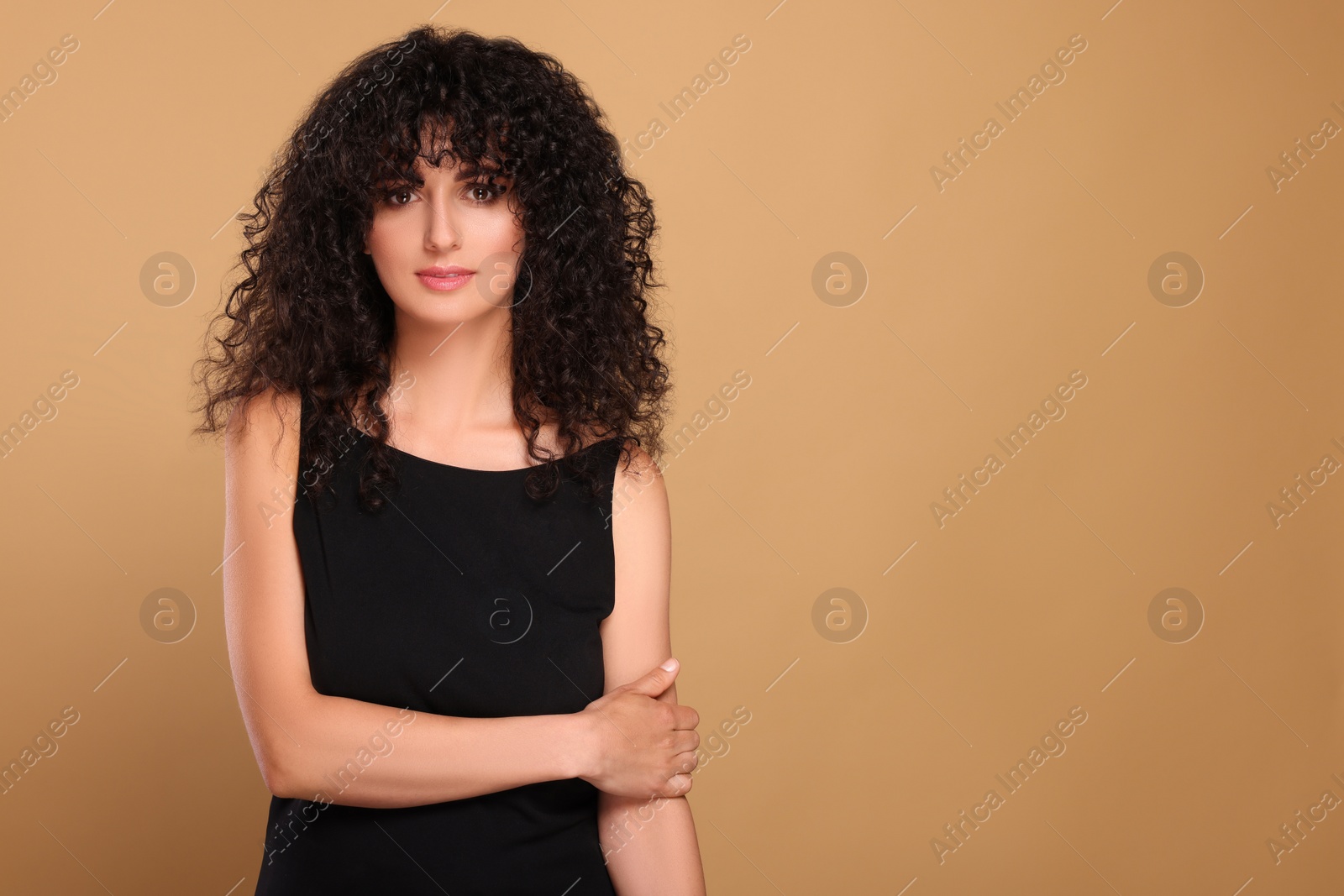 Photo of Beautiful young woman with long curly hair on beige background. Space for text