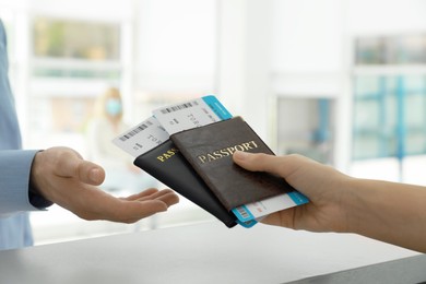 Agent giving passports and tickets to man at check-in desk in airport, closeup