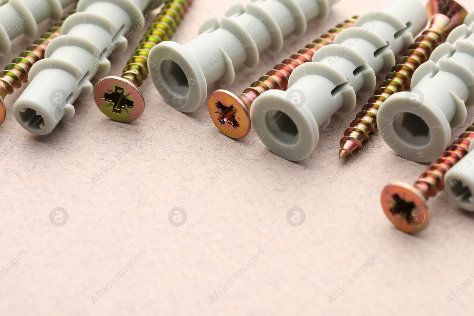 Photo of Many metal screws and dowels on beige textured table, closeup. Space for text