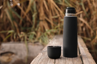 Black thermos and cap on wooden surface outdoors. Space for text