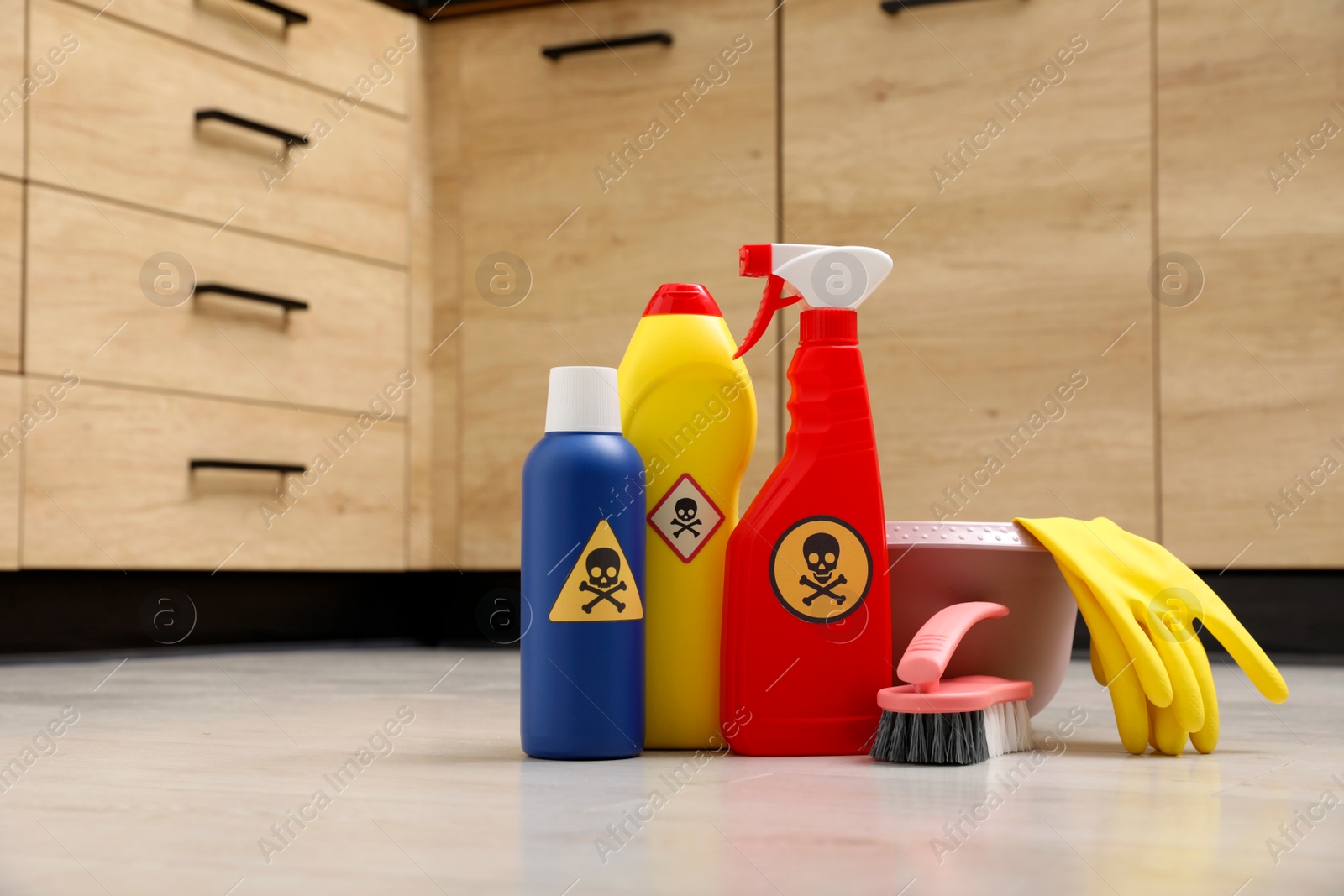 Photo of Bottles of toxic household chemicals with warning signs, gloves and brush on floor indoors, space for text