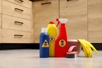 Photo of Bottles of toxic household chemicals with warning signs, gloves and brush on floor indoors, space for text