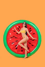 Happy young woman with beautiful suntan, sunglasses and inflatable mattress against orange background