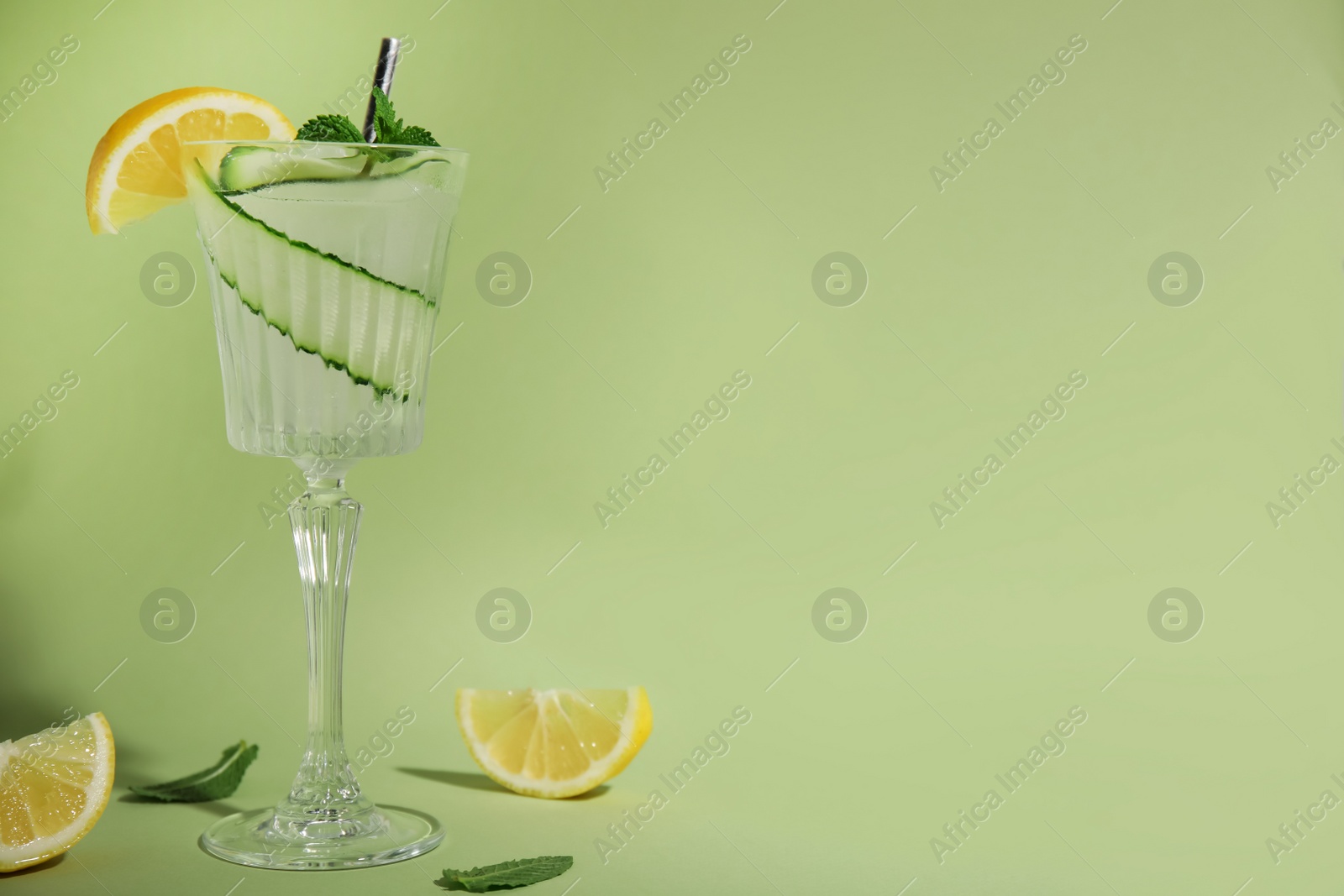 Photo of Glass of tasty fresh cucumber water with mint and sliced lemon on light green background, space for text