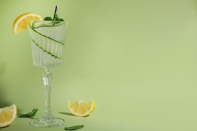 Glass of tasty fresh cucumber water with mint and sliced lemon on light green background, space for text