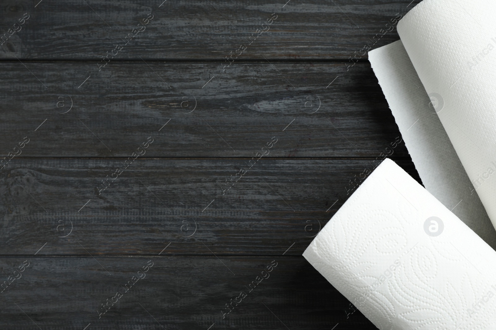 Photo of Rolls of paper towels on black wooden table, top view. Space for text