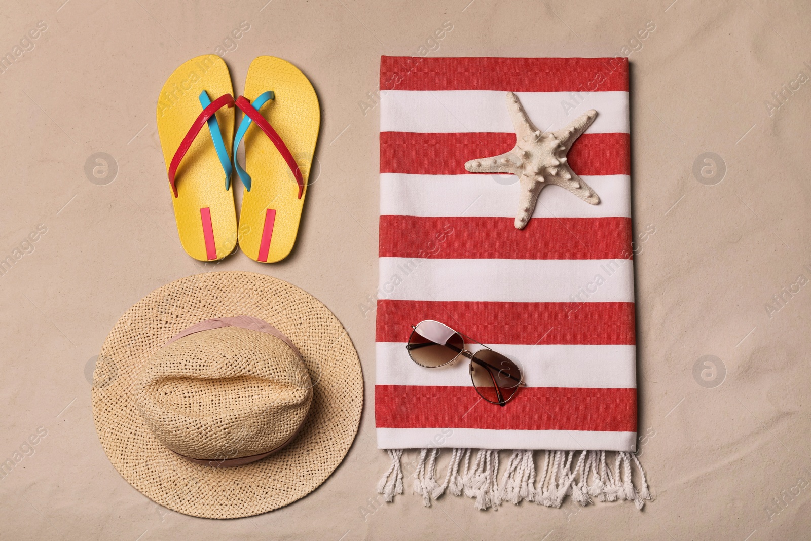 Photo of Beach towel, hat, sunglasses, starfish and flip flops on sand, flat lay