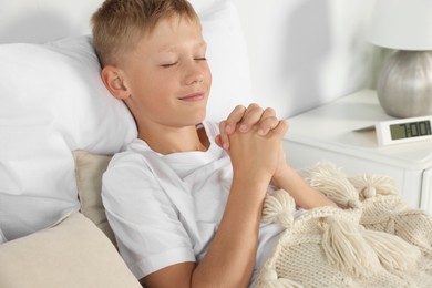 Boy with clasped hands praying in bed at home